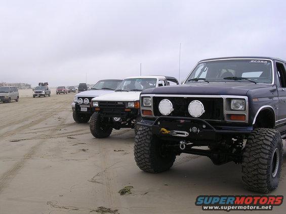 Dark blue pickup truck front view with winch, off-road lights, and large tires on a sandy beach