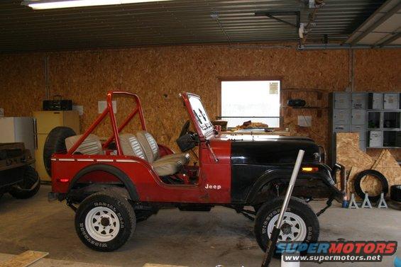 Red and black Jeep CJ in garage, roll bar, spare tire on back