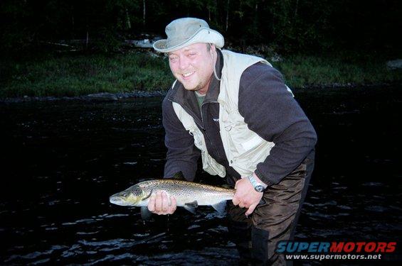 Man in fishing gear holding a large salmon in a river