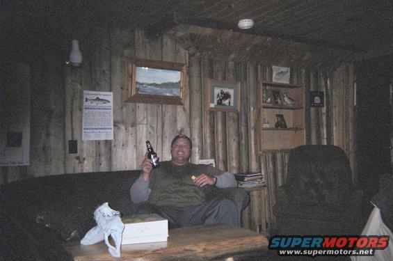 Man sitting on couch in wood-paneled room, holding a beer bottle