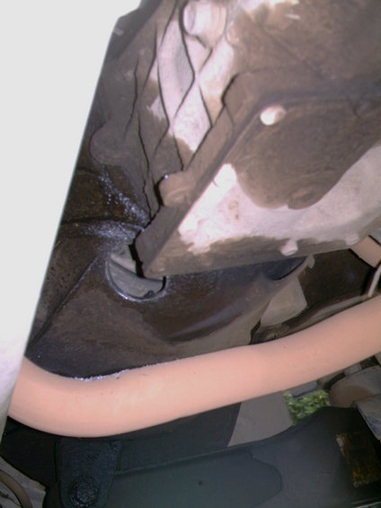 Underside of a vehicle showing a greasy, possibly leaking transmission or oil pan and exhaust pipe