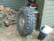 1994 Jeep YJ - A single off-road tire rests beside a building, surrounded by dry grass and debris.