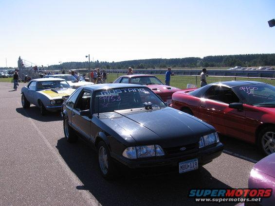 Black 1989 Ford Mustang with racing decals on windshield, parked on asphalt