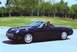 2002 Ford Thunderbird - A black 2002 Ford Thunderbird convertible is captured in motion on a paved surface with a grassy area and trees in the background.