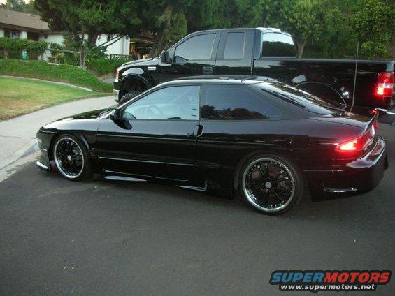 Black 1994 Ford Probe with custom wheels, parked next to a black pickup truck