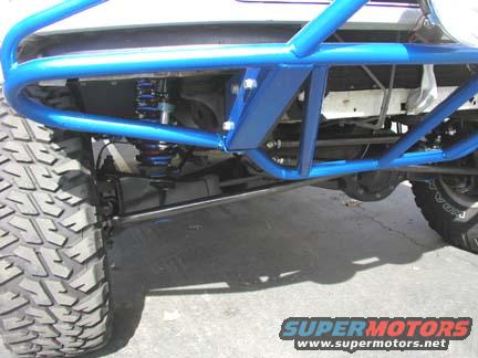 Close-up of off-road vehicle suspension with blue roll cage and large tire. "SUPERMOTORS www.supermotors.net" text visible