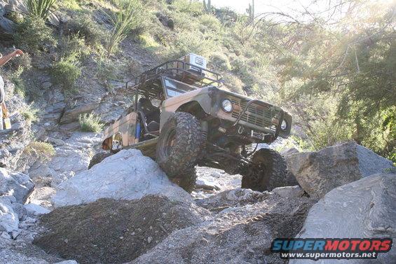 1966 Ford Bronco with roof rack and off-road tires navigating rocky terrain