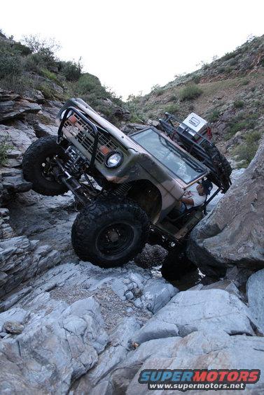1966 Ford Bronco with camouflage paint climbing over rocks on a trail