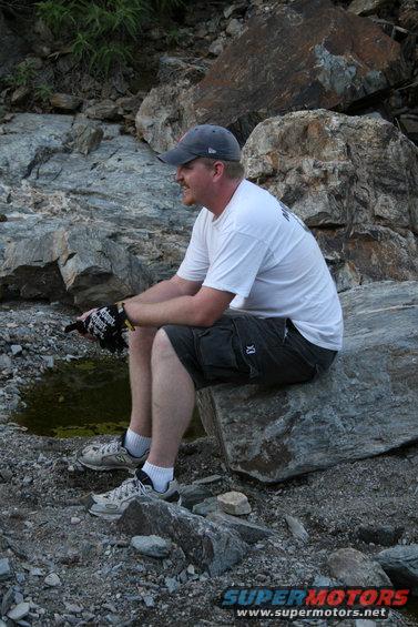 Man wearing a cap, t-shirt, and shorts sits on a large rock outdoors