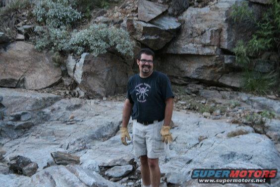 Man in t-shirt and shorts stands in a rocky, outdoor environment