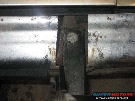 Close-up of a rusty metal bracket bolted to a vehicle's frame, showing signs of wear and tear