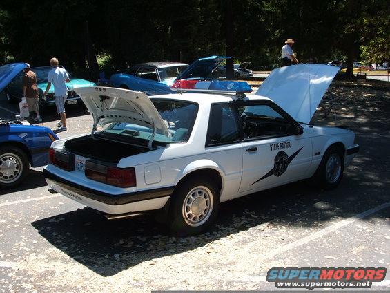 White Ford Mustang police car with trunk and hood open. "State Patrol" text visible on door