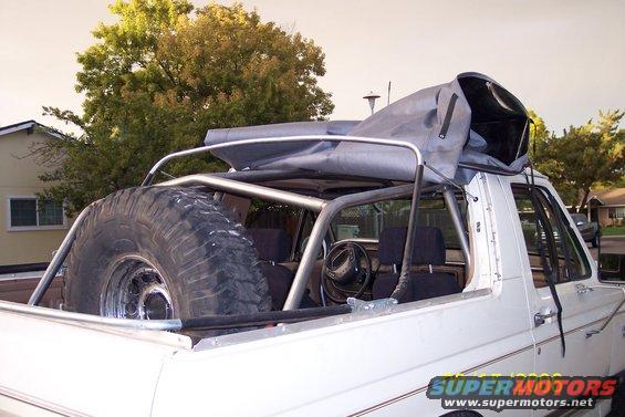 1989 Ford Bronco interior with roll cage, spare tire in bed, and soft top frame
