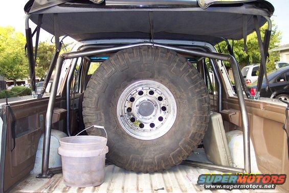 Interior view of a vehicle's cargo area with a large spare tire and custom roll cage