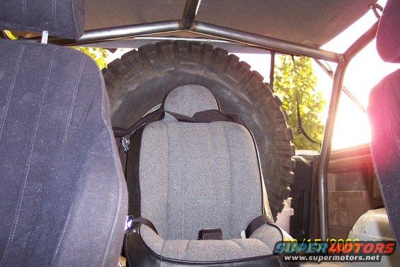 Interior view of a vehicle with a roll cage, spare tire, and seats. A watermark reads 'SUPERMOTORS.NET'