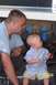 1989 Ford Bronco - A man and a baby examine the underside of a vehicle, with visible wiring and blue tape.