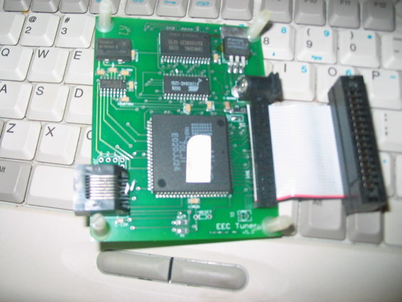 Electronic circuit board labeled 'EEC Tuner' with various chips and connectors, resting on a computer keyboard