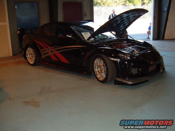 Black sports car with red and silver graphics on the side, hood open showing the engine