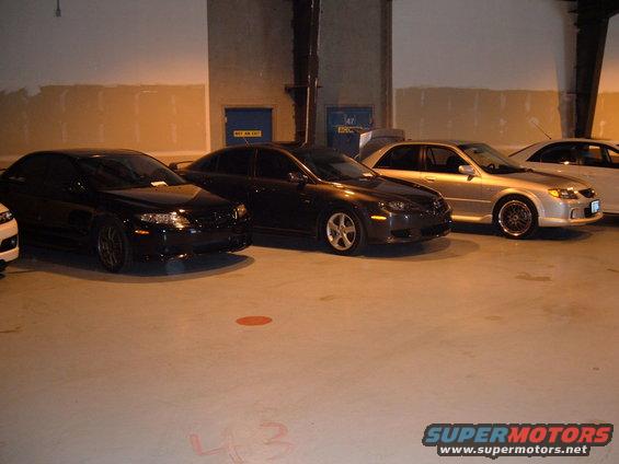 Three sedans parked in a garage, one silver, one dark gray, one black