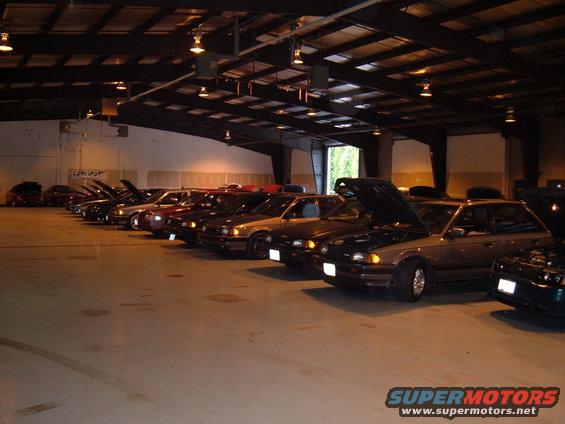 Several Mazda 323 hatchbacks parked inside a warehouse, hoods up on some