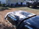 1988 Ford Bronco - A camouflaged Bronco hardtop lies on the ground next to another vehicle part. The hardtop has several stickers on its window.