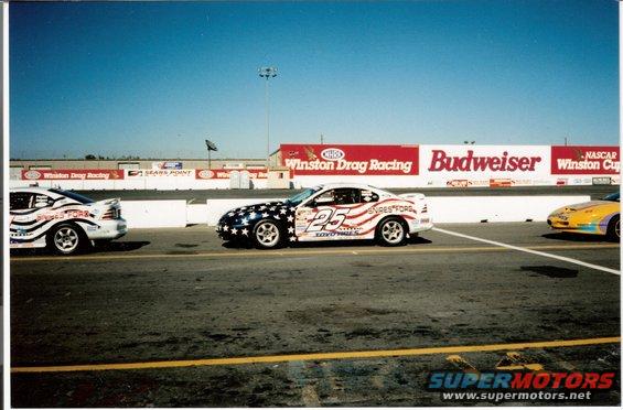 Two race cars, one with stars and stripes livery and number 25, on a drag strip with sponsor banners in the background