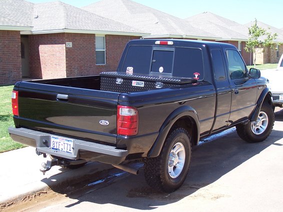 Black Ford Ranger pickup truck parked on street, rear view. Has a toolbox in the bed