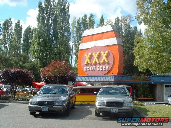 Two sedans parked in front of a XXX Root Beer stand. One is a Mercury Grand Marquis, the other is a Ford Crown Victoria