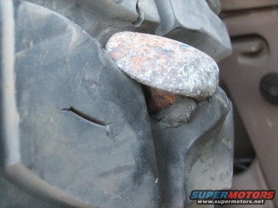 Close-up of a tire with a rusty nail embedded in its tread, showing a cut in the rubber