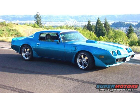 Blue coupe with hood scoop parked on a road with a scenic overlook in the background