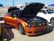 2002 Ford Mustang - This orange Mustang has its hood open, revealing the engine bay, at an outdoor car show.