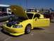 2002 Ford Mustang - A yellow 2002 Ford Mustang is displayed with its hood and driver door open at a car show.