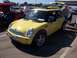 2002 Ford Mustang - A yellow Mini Cooper is parked at a car show, with a surfboard on its roof and trunk open.