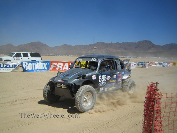 Off-road buggy with number 555 kicking up dust on a sandy track