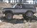 1985 Ford Bronco - A two-tone Ford Bronco navigates a challenging off-road course, with its tires on uneven ground.