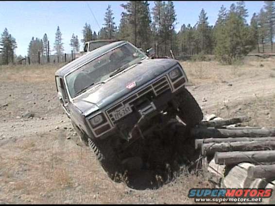 Dark blue SUV with lifted suspension and off-road tires navigating a log obstacle