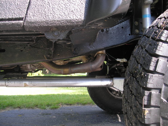 Undercarriage of a vehicle showing exhaust pipes, frame, and tire