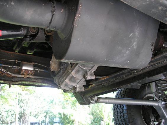 Underbody view of vehicle drivetrain and exhaust system. Visible parts include driveshaft, muffler, and fuel filter