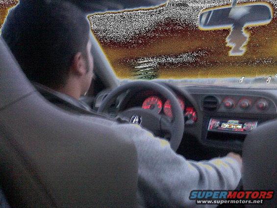 Interior view of a car with a driver, red illuminated gauges, and a car stereo