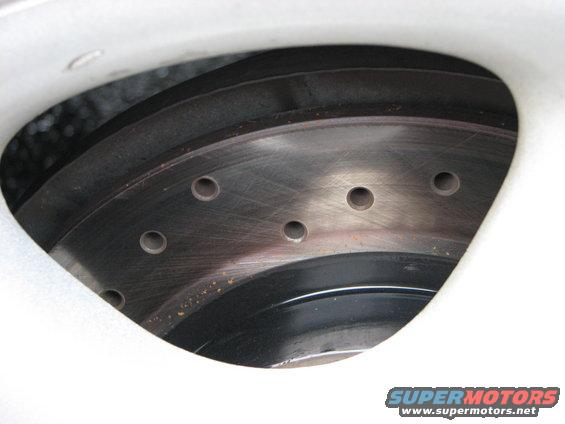 close-up of a drilled brake rotor with a white wheel rim visible