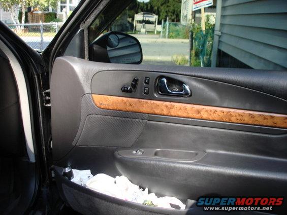 Interior of a car door showing the armrest, door handle, window controls, and a storage pocket with items inside