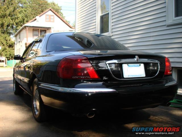 Black Lincoln Continental parked in driveway, rear view. License plate is visible