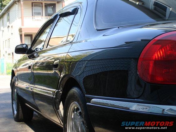 Black sedan parked outside a house, showing the rear passenger side door and quarter panel