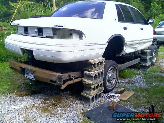 White Mercury Grand Marquis on cinder blocks, missing rear bumper and taillights