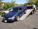 1992 Ford Taurus - A blue sedan is being loaded onto a tow truck, with other vehicles visible in the background.