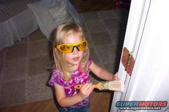Child wearing yellow safety glasses paints a white door