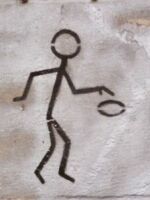 Stick figure graphic painted on a wall, holding a flat oval object