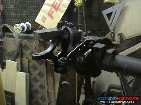 Close-up of a black metal suspension component, possibly from a vehicle axle, in a workshop setting