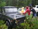 1990 Ford Bronco - Several people in rain gear surround a dark green SUV, with other vehicles visible in the background.