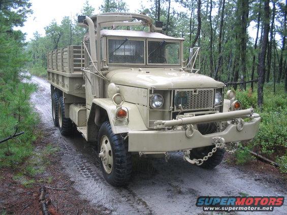 tan military truck on a dirt road in the woods